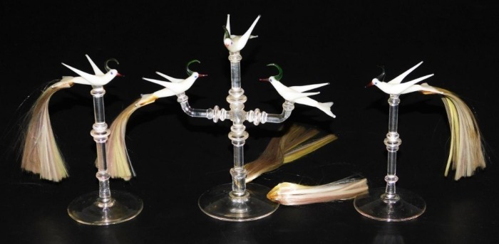 A set of three 20thC Continental glass table ornaments, each modelled as a white bird with hair formed tail feathers, raised on a turned glass stand and circular foot, comprising two single birds and a three bird group. (3)
