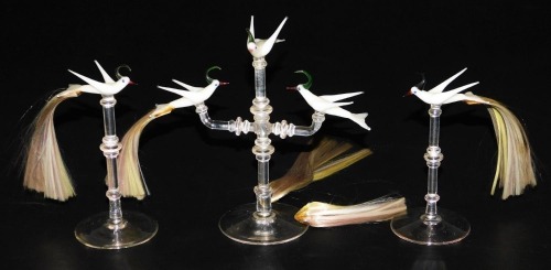 A set of three 20thC Continental glass table ornaments, each modelled as a white bird with hair formed tail feathers, raised on a turned glass stand and circular foot, comprising two single birds and a three bird group. (3)