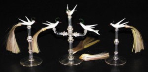 A set of three 20thC Continental glass table ornaments, each modelled as a white bird with hair formed tail feathers, raised on a turned glass stand and circular foot, comprising two single birds and a three bird group. (3)