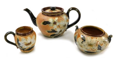 A late 19thC Royal Doulton stoneware three piece tea set, modelled by Alice Ritchin, tube line decorated with flowers and leaves against a chine ground, incised and impressed marks, comprising teapot, cream jug and sugar bowl.