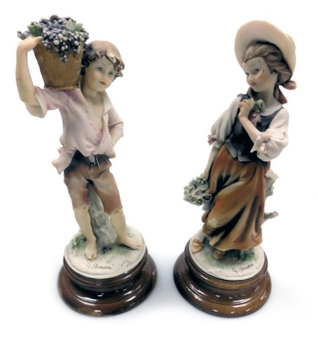 A pair of Capodimonte figures, modelled by G Armani, of a girl with a basket of flowers, and a boy holding a basket of grapes on his shoulder, raised on wooden bases, incised and painted marks, 28cm high.