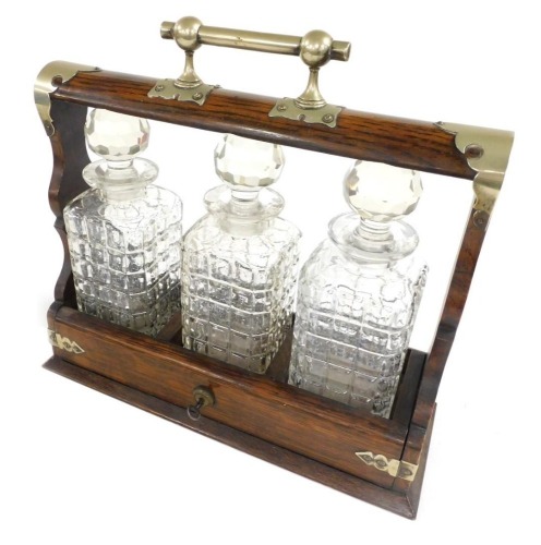 An early 20thC oak and plate mounted tantalus, with three cut glass decanters and stoppers, with key, 37cm wide.