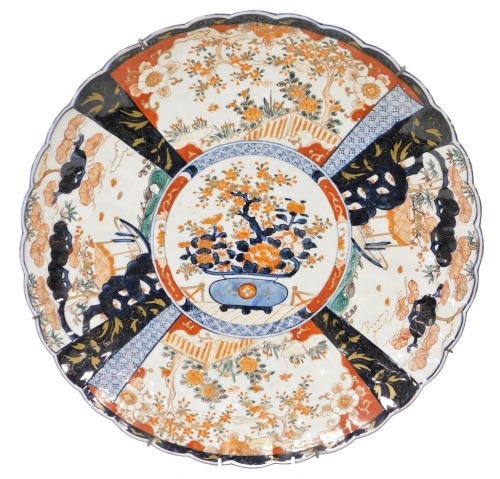 A Meiji period Japanese Imari charger, of fluted form, decorated centrally with a jardiniere of flowers, within fan shaped panels of trees and flowers in a garden, 46cm wide.