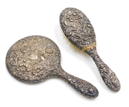 An Edward VII silver backed hairbrush, embossed with flowers and foliate scrolls, Birmingham 1901, together with a silver backed hand mirror, embossed with striking flowers, and rococo scrolls, vacant shield reserve, Birmingham 1905. (2)