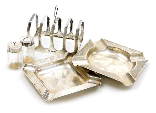 A George V silver four division toast rack, Sheffield 1934, George VI silver ashtray with engine turned decoration, Sheffield 1938, further ashtray of plain form, Birmingham 1962, 5.11oz, and a pair of cut glass salt and pepper shakers, with silver screw 