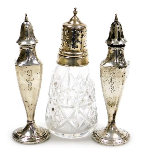 A pair of early 20thC loaded silver sifters or pepperettes, monogram engraved, stamped sterling, 17cm high, 4.01oz all in, together with a cut glass sugar sifter, with silver mount and lid, Birmingham 2000. (3)