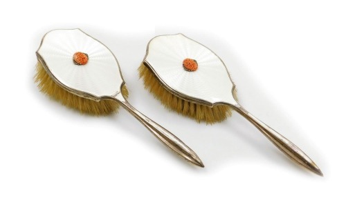 A pair of George V silver and white guilloche enamel hairbrushes, with engine turned decoration, set centrally with a coral and marcasite floral ornament, Birmingham 1934.
