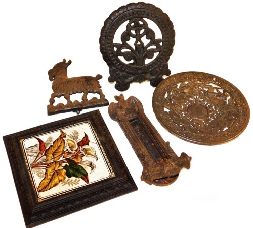 A group of Victorian cast iron, comprising a cast iron door knocker with letters aperture, Coalbrookdale cast iron dish top, cast iron trivet, doorstop top formed as a standing goat, and a pottery tile in a cast iron frame, as a kettle stand. (5)