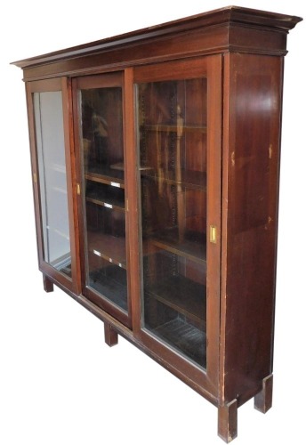 An early 20thC mahogany office bookcase, the outswept pediment over three sliding doors enclosing four long and four short shelves, raised on stiles, 167.5cm high, 193cm wide, 41.5cm deep.