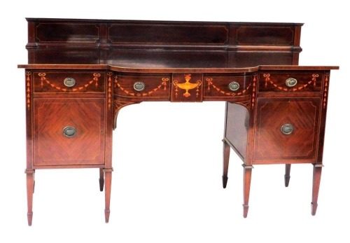 An early 20thC Sheraton revival mahogany bow front sideboard, with a panelled back, above a bow fronted door inlaid with an urn and festoons of harebells, flanked by two drawers similarly decorated above a pair of panelled doors, raised on tapering square