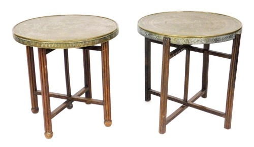 Two early 20thC Benares brass tray top tables, engraved with Arabic script and arabesques, each raised on fluted legs united by an X frame stretcher, 58cm high, 60cm wide.