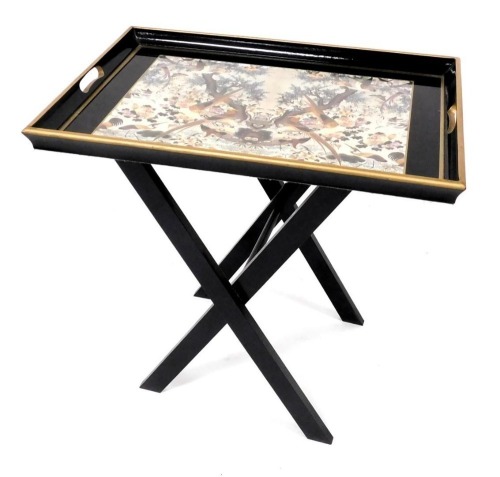 A Lady Clare ebonised drinks tray on a folding stand, the twin handled tray printed centrally with exotic birds, 57cm high, 55cm wide.