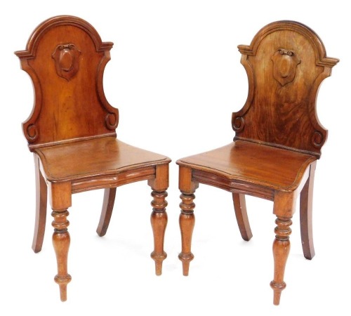 A pair of Victorian mahogany hall chairs, the shaped back with a carved shield, above a serpentine seat, raised on turned legs.