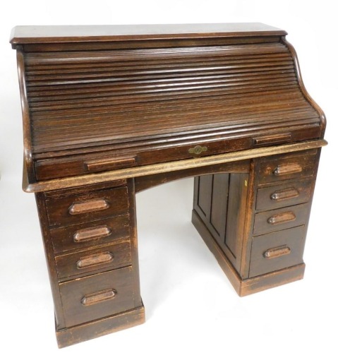 A Victorian oak roll top, the tambour top opening to reveal recesses, with a central cushion drawer flanked by eight graduated pedestal drawers, raised on plinth bases, 118cm high, 121cm wide, 68cm deep.