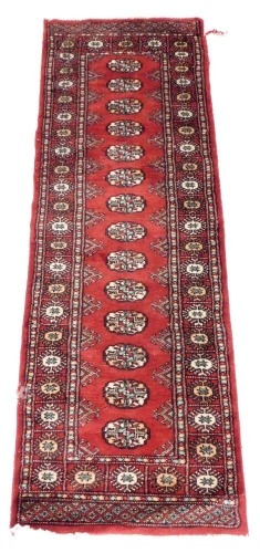 A Bokhara red ground runner, decorated to the central field with fourteen medallions, within repeating floral borders, 188cm x 63cm.