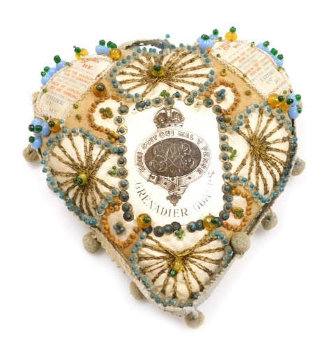 A WWI period Grenadier Guards sweetheart cushion, of heart shaped design with woven silk text and bead work and braided decoration with pompom border.