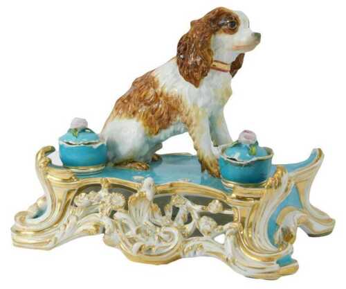 A 19thC Jacob Petit (Fontainebleau) porcelain inkstand, of scrolling and floral encrusted form, in blue and white with gilt highlights, surmounted by figure of a Spaniel, with two porcelain lidded inkwells, signed JP, 30cm high. (AF)