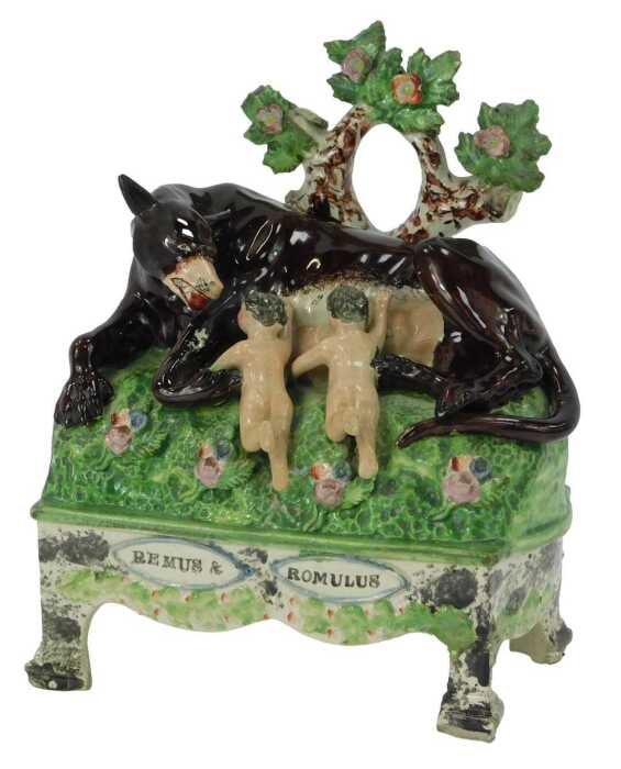 An early 19thC Staffordshire figure group, modelled as Remus and Romulus suckling a she wolf, on a titled table base, 21.5cm high. (AF)