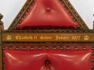An Elizabeth II Silver Jubilee oak throne chair, with red leather upholstery, and carved and raised back, with crested and button decoration bearing gilded inscription, 150cm high, 69cm wide, 70cm deep. - 3