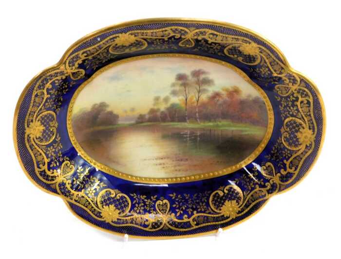 A Paragon porcelain shaped oval dish, titled 'Autumn Leaves, After Parton', decorated centrally with lake scene and trees signed F Micklewright, with a Royal blue border, gilt heightened, printed marks, 25cm wide.