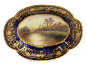 A Paragon porcelain shaped oval dish, titled 'Autumn Leaves, After Parton', decorated centrally with lake scene and trees signed F Micklewright, with a Royal blue border, gilt heightened, printed marks, 25cm wide.