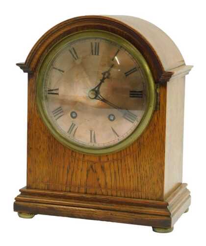 An early 20thC oak cased mantel clock, the silvered circular dial bearing Arabic numerals, eight day, the case of arched form, the moulded base on compressed brass feet, 29cm high.