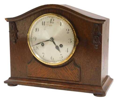 An early 20thC oak cased mantel clock, the silvered circular Arabic numeral dial with eight day movement, the case with a shaped top and applied decoration, on four compressed bun feet, 25cm high.