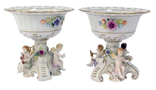 A pair of 20thC Schierholz porcelain centrepieces, each bowl with a pierced border decorated with handpainted and relief decorated flowers, above a floral encrusted stem, on scrolling gilt heightened base interspersed with cherubs playing musical instrume