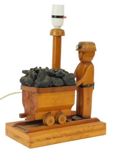 A treen table lamp, modelled as a miner pushing a trolley containing coal, 34cm high.
