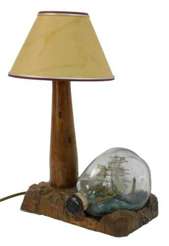 A 20thC oak desk lamp, modelled as a light house with shade, on a carved base, together with a ship in glass bottle titled The Phantom Sleeper, 38cm high.