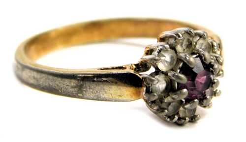 A fashion ring, the floral cluster central set with purple stone, surrounded by paste stones, on silver collared base metal band, ring size N&frac12;.