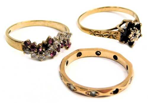 Three dress rings, comprising a 9ct gold half hoop dress ring, of twist design, set with garnets and czs, ring size K&frac12;, sapphire and diamond cluster ring, ring size L, and an eternity ring set with cz stones, yellow metal unmarked, ring size M&frac12;, 4.2g all 