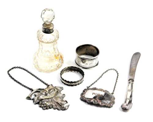 A George V cut glass scent bottle and stopper, with silver collar, Birmingham 1911, cake knife with silver pistol handle, Sheffield 1911, two silver napkin rings, Continental brandy label, and a Sheffield plate port label. (6)