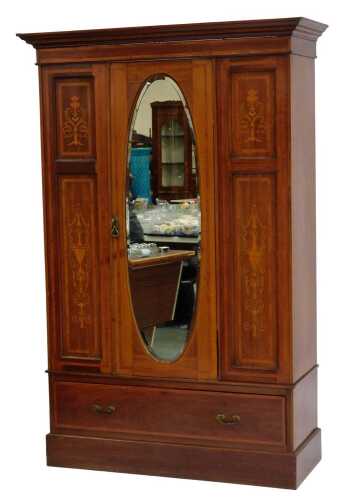 An Edwardian mahogany and marquetry wardrobe, the top with a moulded cornice above an oval mirrored door, flanked by urn and scrolling inlaid motifs, the hinged door enclosing various hanging hooks, the wardrobe with drawer to base, on plinth, 198cm high,