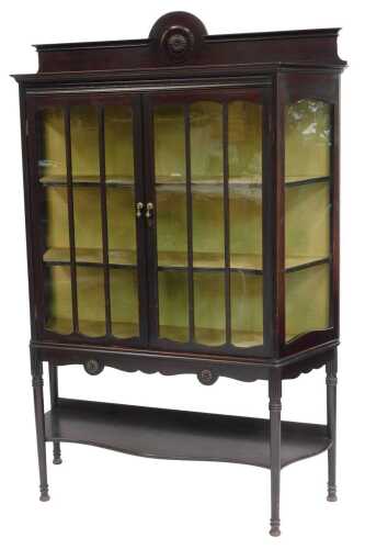 An Edwardian mahogany display cabinet, the top with a moulded edge and raised back, above two glazed panelled doors and glazed sides enclosing three shelves, with under tier raised on cylindrical part fluted legs, 171cm high, 112cm wide, 40cm deep.