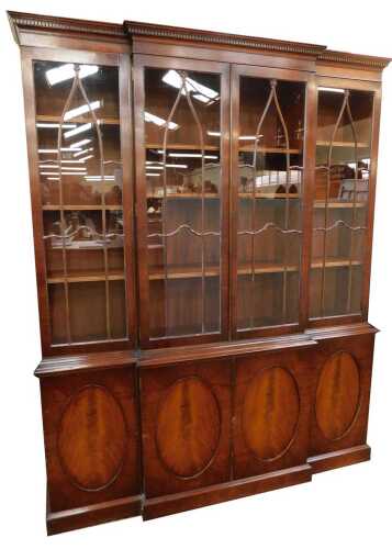 A 20thC mahogany breakfront bookcase in Georgian style, the top with a dentil moulded edge, above four glazed doors, the base of four cupboards, each with oval roundel decoration, on plinth, 215cn high, 175cm wide, 44cm deep.