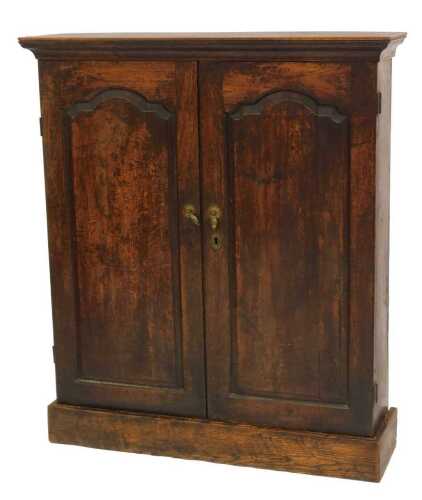 A Georgian oak two door cabinet, the top with a rounded edge above two panelled doors with brass drop handles enclosing three shelves, on a plinth base, 113cm high, 97cm wide, 27cm deep.