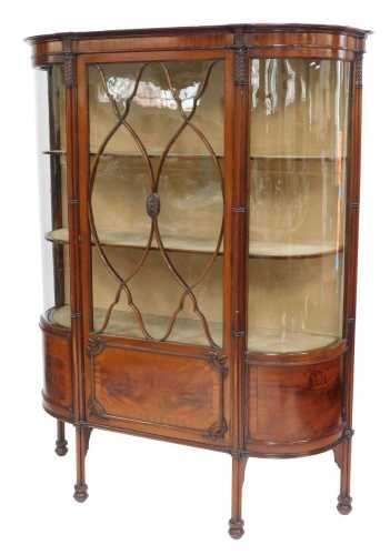 An Edwardian mahogany display cabinet, the top with a moulded edge above floral rosette and leaf carved columns with an astragal glazed door enclosing three curved shelves with two curved glass side panels, raised on multiple united column legs, on compre