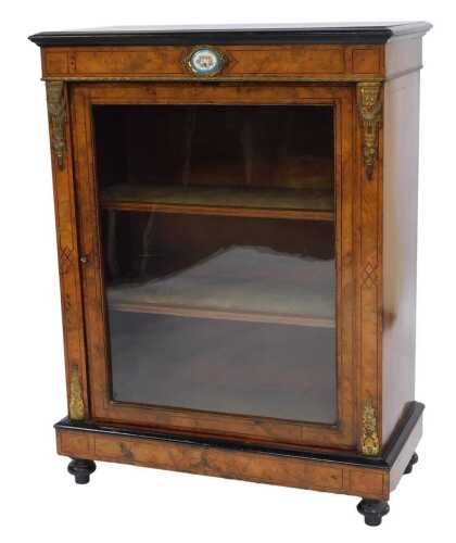 A Victorian walnut and ormolu mounted pier cabinet, the top with a moulded ebonised edge above a hand painted floral porcelain roundel, the glazed door enclosing three shelves, on compressed bun feet, 105cm high, 83cm wide, 40cm deep.
