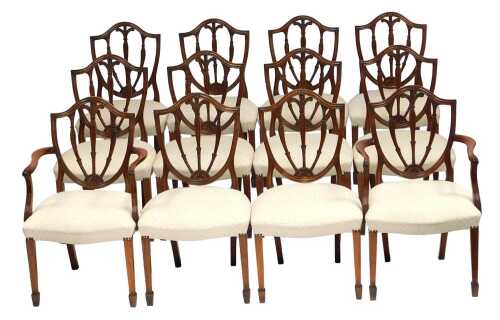 A set of twelve Hepplewhite mahogany dining chairs, each with a shield back with Prince of Wales feathers decoration, overstuffed seats, on square tapering legs with spade feet, comprising a pair of carvers and eight chairs.