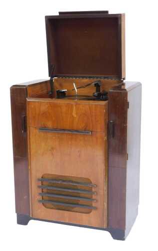 A mid century walnut and mahogany Bush RG4 radiogram, the hinged lid enclosing a Garrard Model RC65 turntable, over a fall enclosing dial and switches, flanked by two cupboards to hold records, 98cm high, 72cm wide, 41cm deep.
