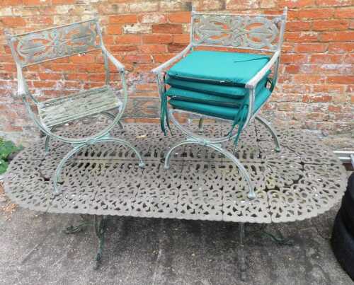 A cast iron garden table, the pierced oval top with four chairs, each florally decorated, the table 70cm high, 210cm wide, 96cm deep.