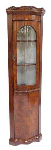 A 20thC mahogany and burr wood standing corner cabinet, the top with a scroll and leaf carved edge above an arched glazed door enclosing three shelves, the base with cupboard, on a shaped plinth base, 193cm high, 48cm wide, 40cm deep.