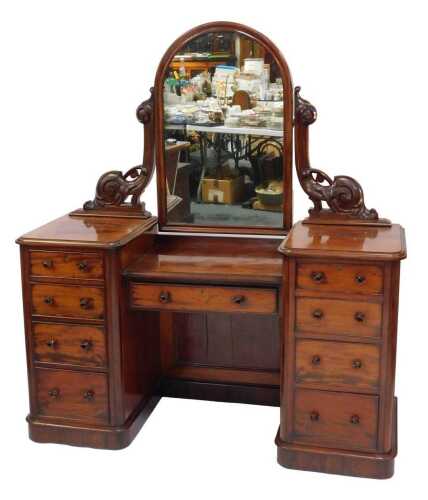 A Victorian figured mahogany mirror back dressing table, the arched mirror on scrolling and leaf carved supports, with central drawer to base flanked by two pedestals with four short drawers, on plinth, 160cm high, 143cm wide, 54cm deep.