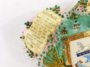A Lincolnshire Regiment sweetheart heart shaped pin cushion, in pink silk with gold braid decoration, and regimental crest, printed ribbon text, 18cm. - 2