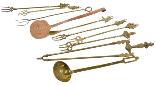 An assortment of toasting forks and other brass and copper implements, including a copper skimmer, brass ladle, etc.