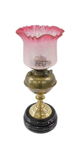 A Victorian brass oil lamp, the later pink cranberry glass shade with floral engraved decoration, on plain brass body, with ebonised circular foot, 48cm high.