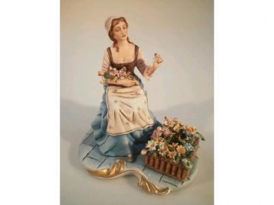 A Capo-di-Monte figure of a young woman selling flowers seated on a basket