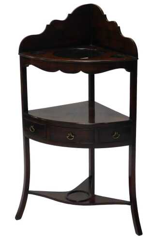 A George III mahogany corner washstand, with a raised back and recesses for bowl and beakers and...