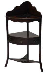 A George III mahogany corner washstand, with a raised back and recesses for bowl and beakers and...